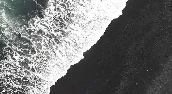 A wave breaks over a black sand beach