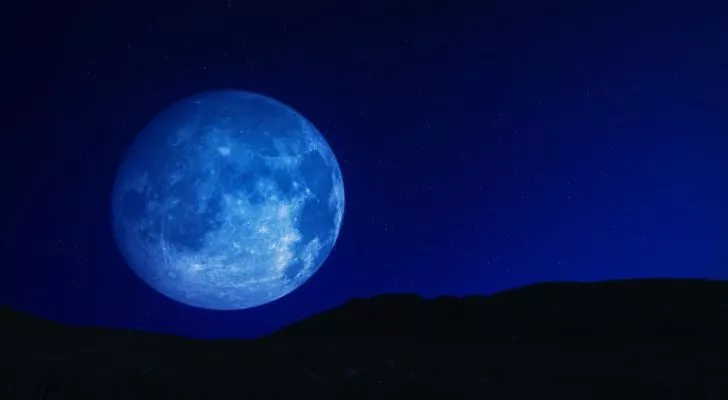 A large blue moon sits just over the horizon at night