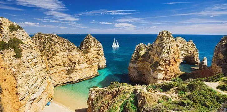 A view of rocky formations on the Algarve coastline, with a white yacht in the background